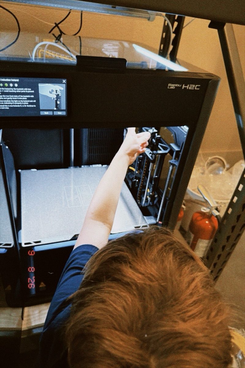 Joseph reaching into the open H2C printer to seat a hotend, the on-screen guide showing the step